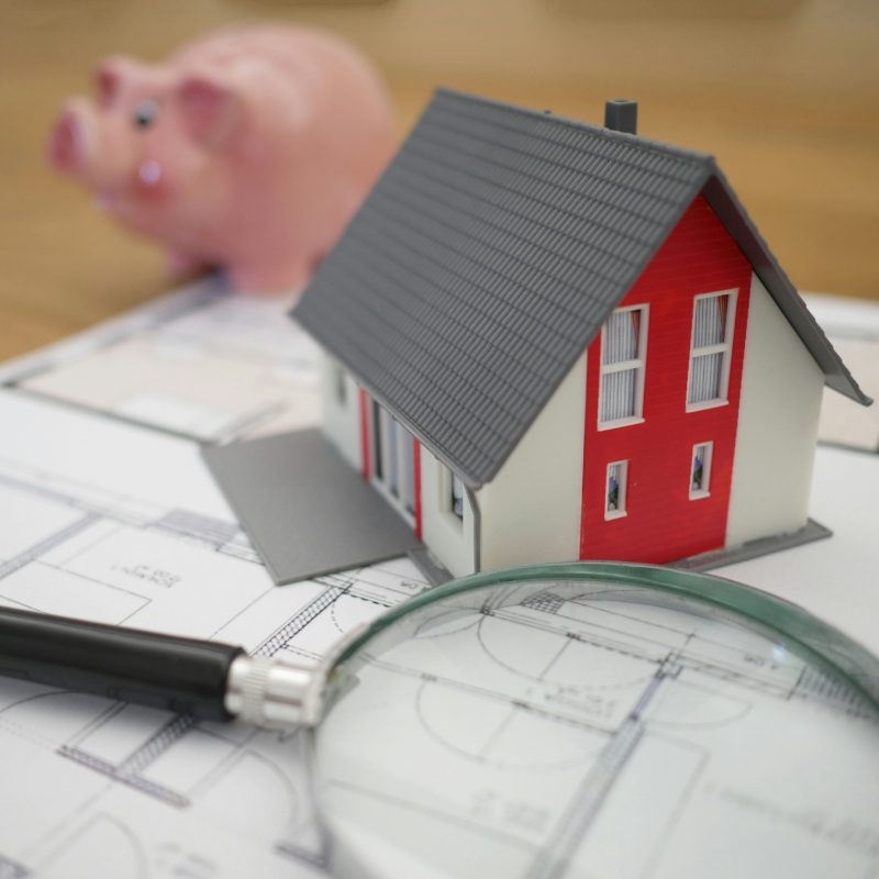 small-scale model house with piggy bank & Magnifying glass on house schematic